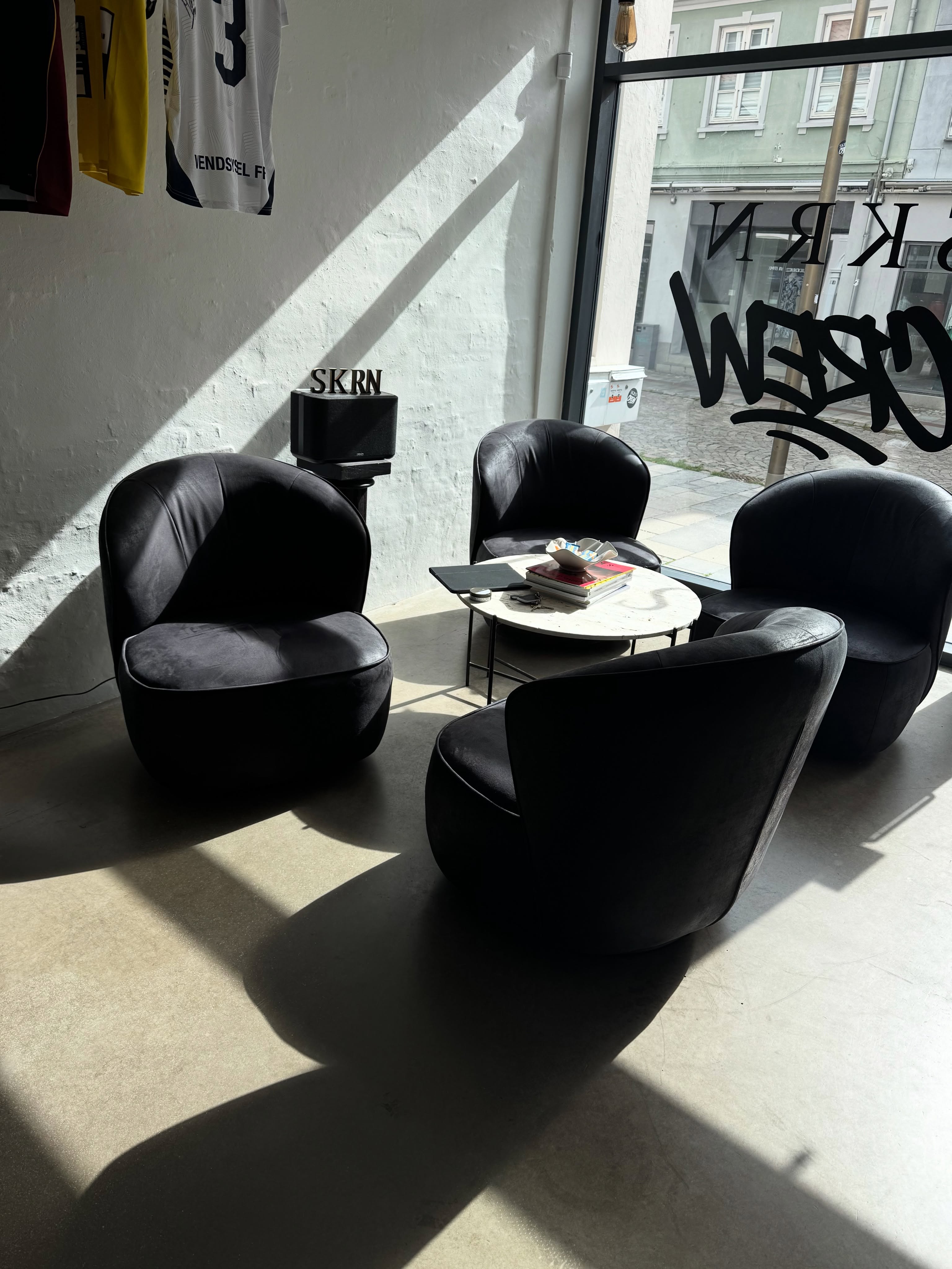 The front room at SKRN.CREW — dark chairs around a low table, a speaker marked SKRN, and the shop window onto the street