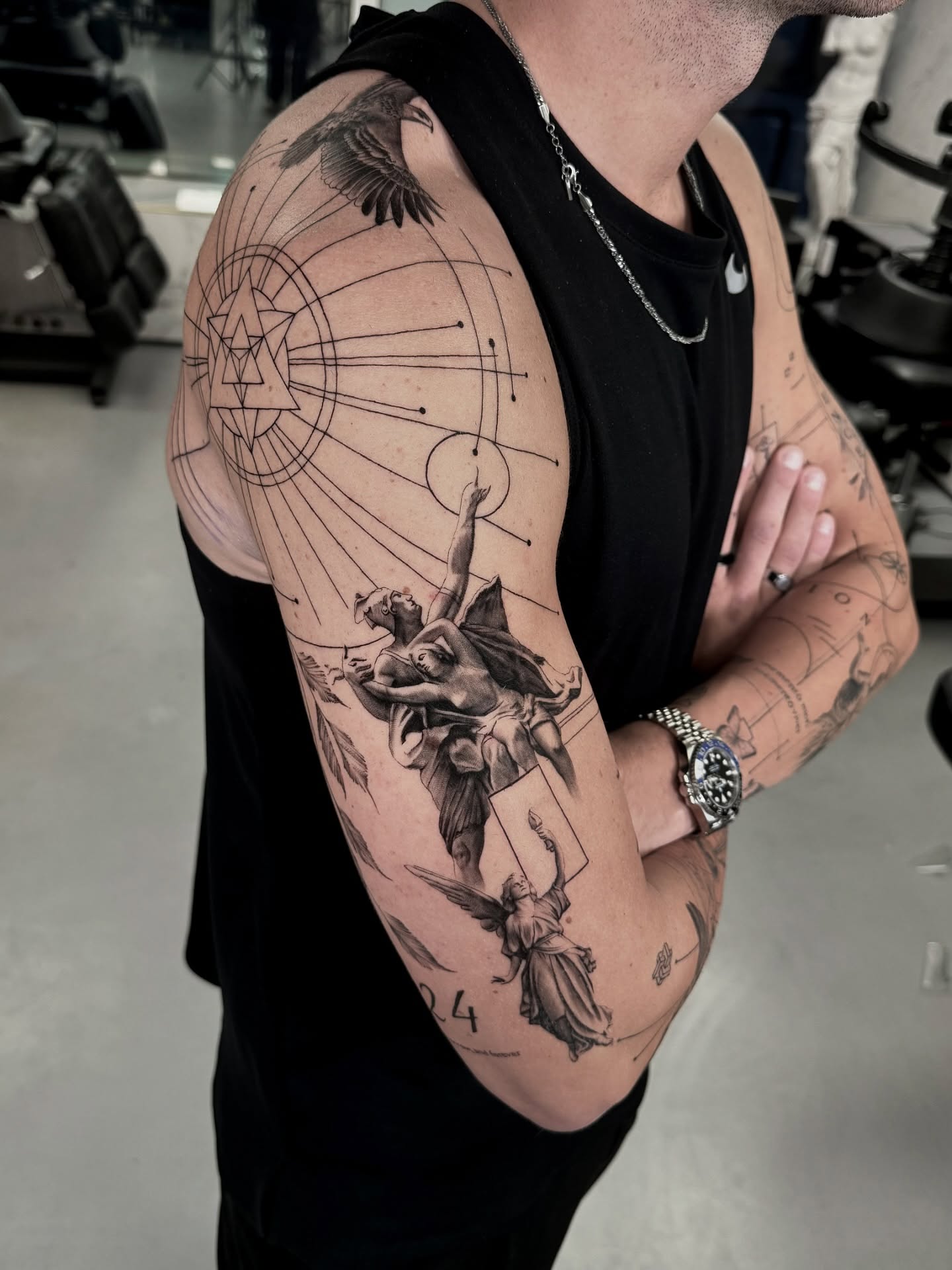 Black and grey composition across shoulder and arm with a radial geometric anchor and several winged figures